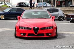 a red alfa coupe parked in front of some cars on the side of the road