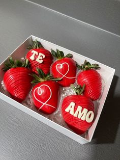 four chocolate covered strawberries in a box with the word amo painted on them