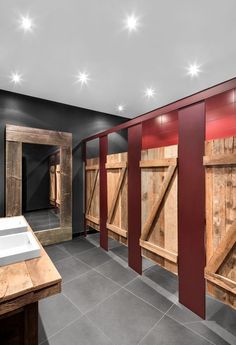 a bathroom with red and black walls, wooden stalls and sinks in the middle of it