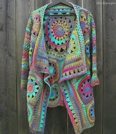 a colorful crocheted jacket hanging on a wooden fence next to a wood wall