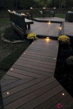 a wooden deck with lights on it and flowers in the grass next to it at night