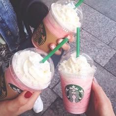 three starbucks drinks with whipped cream and green straws are being held by two people