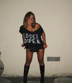 a woman standing in front of a white wall wearing black boots and a t - shirt that says loaded diper