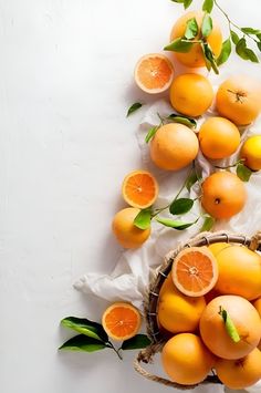 a basket filled with lots of oranges on top of a white table next to green leaves