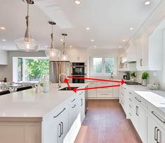 a kitchen with white cabinets and an island in the middle is marked by red arrows