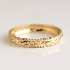 a gold wedding band that has been engraved on the side and is sitting on a white surface