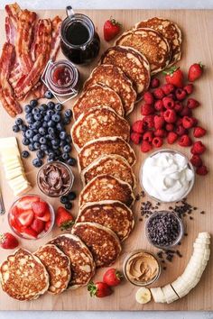 a wooden cutting board topped with pancakes covered in fruit and bacon next to other foods