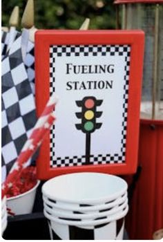 a table topped with lots of white plates and buckets filled with red flowers next to a sign that says fueling station