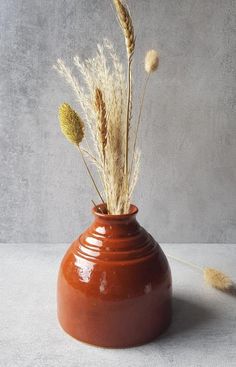 a brown vase with some dry grass in it