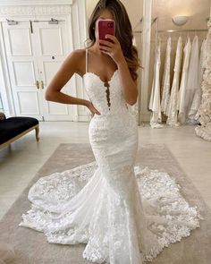 a woman taking a selfie while wearing a wedding dress in a bridal gown shop