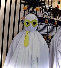 two white ghost costumes with yellow ties and sunflowers on their heads, standing in front of a wall