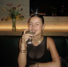 a woman sitting at a table holding a wine glass in front of her face and smiling