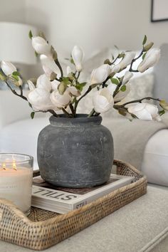 white flowers in a vase on a tray next to a lit candle and some books