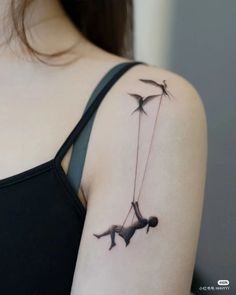 a woman's arm with two birds flying through the air and holding onto a string