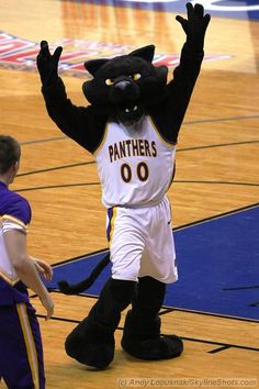 a man in a black and white basketball uniform standing next to a mascot on a court