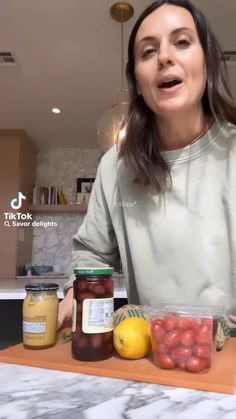 a woman standing at a counter with jars of fruit and vegetables in front of her