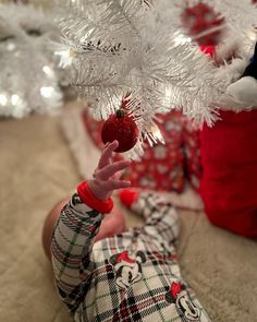 a baby is reaching up to the white christmas tree