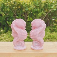 two pink seahorses sitting on top of a wooden table in front of some bushes