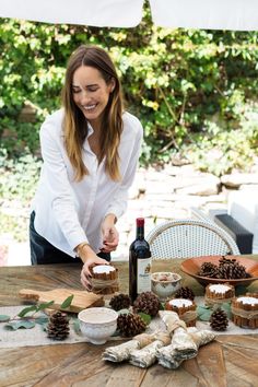 a woman standing over a table with some food and wine bottles on top of it