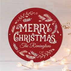 a merry christmas sign on top of a wooden table with white lights around it and greenery in the background