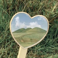 a heart shaped mirror sitting on top of a grass covered field with mountains in the background