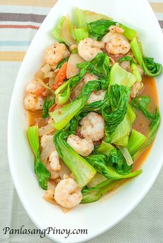 a white bowl filled with shrimp and veggies on top of a striped table cloth