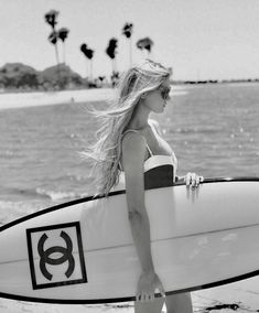 a woman walking on the beach holding a surfboard