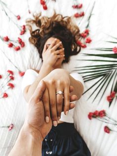 a man and woman holding hands while laying on a bed with red flowers in the background