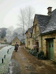 a man walking down a snow covered road next to stone buildings with chimneys and windows