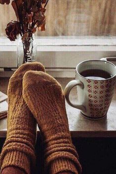 a person's feet in wool socks next to a cup of coffee