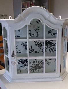 a white display case with flowers painted on the front and side glass doors, sitting on top of a table