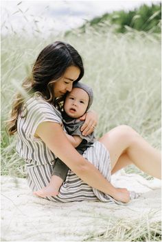 a woman holding a baby in her arms while sitting on the sand at the beach