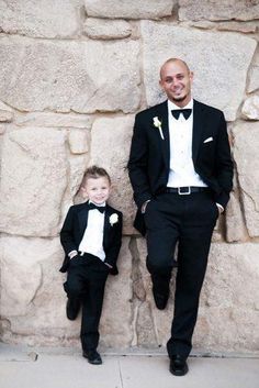 two young boys dressed in tuxedos standing next to a stone wall