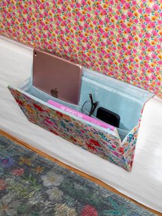 an open laptop computer sitting inside of a storage box on top of a bed next to a wall