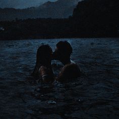 two people are kissing in the water at night, with mountains in the back ground