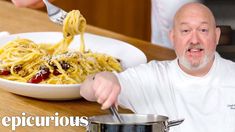 a man holding a ladle with pasta in it while standing next to a plate of food