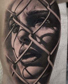 a woman's face behind a barbwire fence tattoo on the right thigh