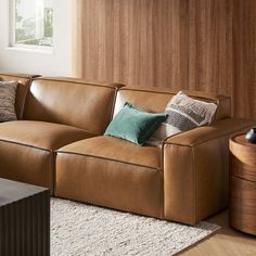 a brown leather couch sitting on top of a white rug next to a wooden table