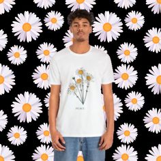 "This adorable T-shirt is the epitome of cute, fun, and light-hearted style. Adorned with charming white daisies, each boasting a vibrant orange center, and the word \"PEACE\" written beneath, it radiates positivity and cheerfulness. Crafted from 100% cotton, this T-shirt promises a soft, comfortable, and durable wearing experience. Its unisex design ensures a flattering fit for everyone, but don't forget to consult the size chart for that perfect fit. To keep this delightful piece looking fresh Cute Organic Cotton Crew Neck T-shirt, Cute White Organic Cotton Tops, White T-shirt With Funny Print For Spring, Casual Spring Shirt With Funny Print, Cute Spring Tops In Organic Cotton, White Organic Cotton Tops For Spring, Spring Graphic Print White T-shirt, Casual T-shirt With Daisy Print For Spring, Casual Screen Print Shirt For Spring