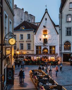 people are walking around in an old town square at dusk, surrounded by buildings and cobblestone streets