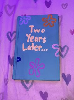 a blue book with two years later written on it sitting on a bed covered in hearts