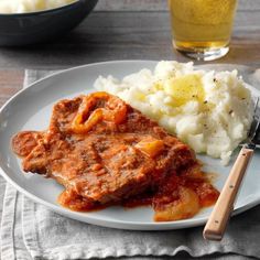 a white plate topped with meat and mashed potatoes next to a glass of beer