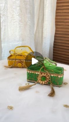 three green and yellow boxes sitting on top of a white table covered in tassels