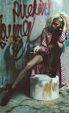 a woman sitting on top of a stool next to a graffiti covered wall and holding an umbrella