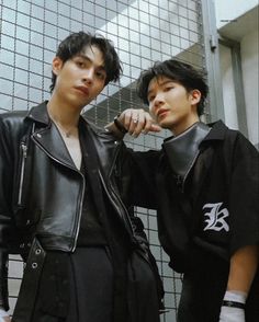 two young men standing next to each other in front of a wall with tiled walls