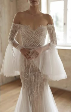 a woman in a white wedding dress standing on a wooden floor with her hands behind her back