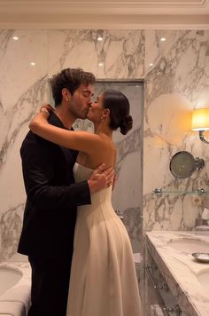 a man and woman are kissing in front of a bathroom mirror, with marble walls