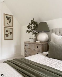 a bedroom with white walls and green linens on the bed, two framed pictures above it