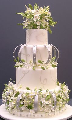 a three tiered wedding cake with white flowers and ribbons on the top, sitting on a table