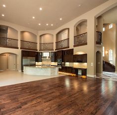 an empty living room with wood flooring and large open kitchen area in the middle